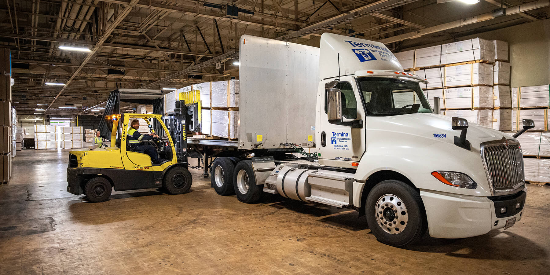 warehouse employee using forklift to load wood products on to a flatbed truck